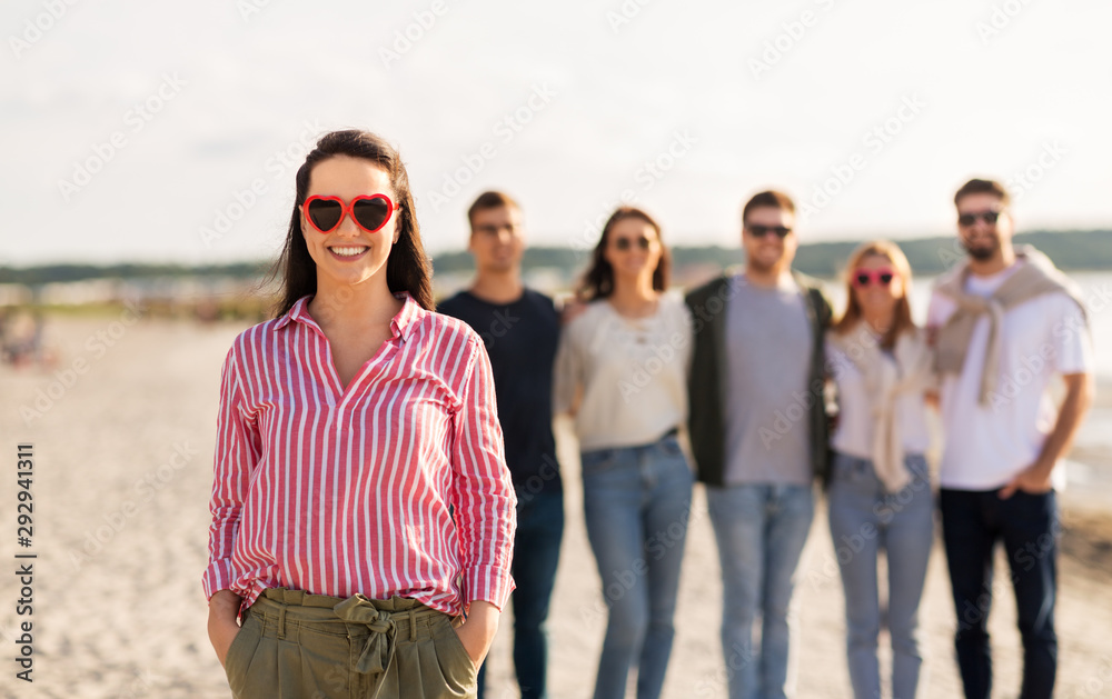 friendship, valentine's day and people concept - happy woman in heart-shaped sunglasses with group of friends on beach in summer friendship, valentine's day and people concept - happy woman in heart-shaped sunglasses with group of friends on beach in summer