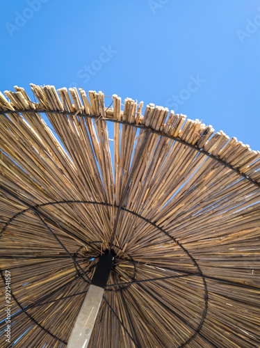 Cone of a straw parasol against clear blue sky. Upward view of the canopy of a beach sunshade made of reed.