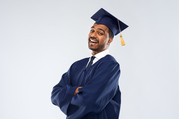 education, graduation and people concept - happy smiling indian male graduate student in mortar board and bachelor gown over grey background