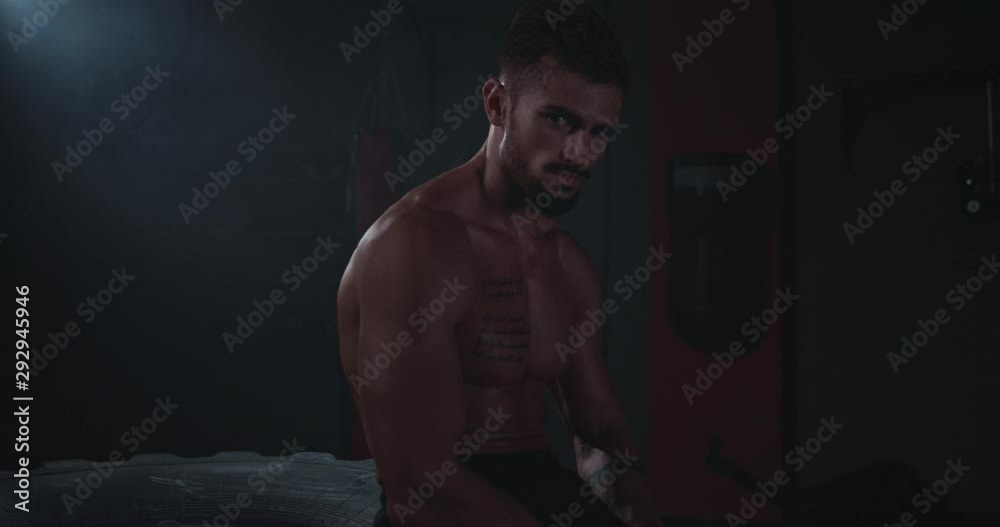 Brutal string fit body guy after his hard workout training sitting in the tire looking to the camera tired and sweating in a cross fitness class Brutal string fit body guy after his hard workout training sitting in the tire looking to the camera tired and sweating in a cross fitness class
