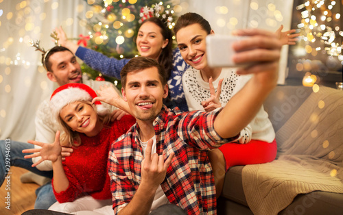 celebration and holidays concept - happy friends with glasses celebrating christmas at home party and taking selfie by smartphone