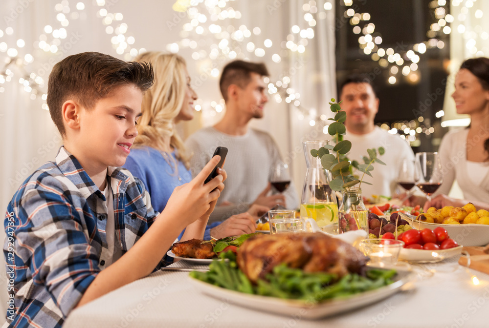 technology, holidays and people concept - happy boy with smartphone having family dinner party at home