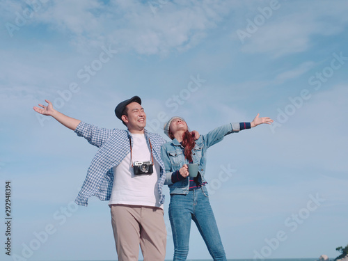 Happy Asian couple raising hands together with nature background, sunny day.