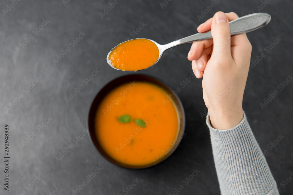 food, eating and new nordic cuisine concept - close up of hands with bowl of pumpkin cream soup and spoon on stone table food, eating and new nordic cuisine concept - close up of hands with bowl of pumpkin cream soup and spoon on stone table