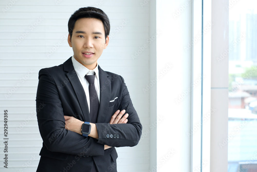 Asian businessman is wearing a black suit ,smiling and standing with arms crossed,white office,young businessman,finance,Intelligent and confident people,Successful leader/Management/finance Asian businessman is wearing a black suit ,smiling and standing with arms crossed,white office,young businessman,finance,Intelligent and confident people,Successful leader/Management/finance