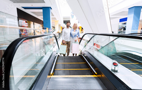 Couple Standing Hugging On Escalator Holding Shopping Bags In Mal