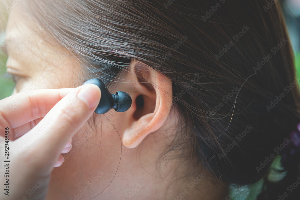 Close up of woman is using the black true wireless earbuds by hand to put in ear and control - obrazy, fototapety, plakaty 