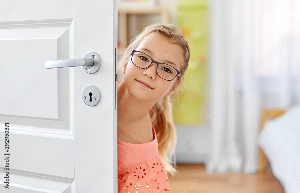 childhood, fun and people concept - happy smiling beautiful girl in glasses behind door at home