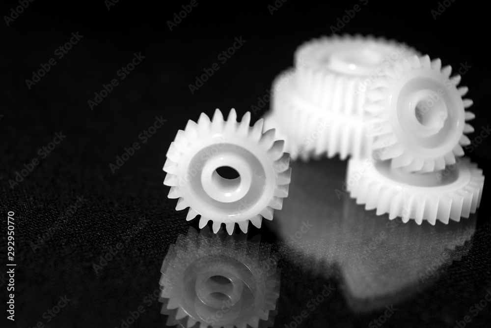 Several white plastic gears on a black mirror background. Mechanical repair. Fix. Reflection. Repair shop. Cogwheels. Elements of a large mechanism. Harmonious work. Several white plastic gears on a black mirror background. Mechanical repair. Fix. Reflection. Repair shop. Cogwheels. Elements of a large mechanism. Harmonious work.