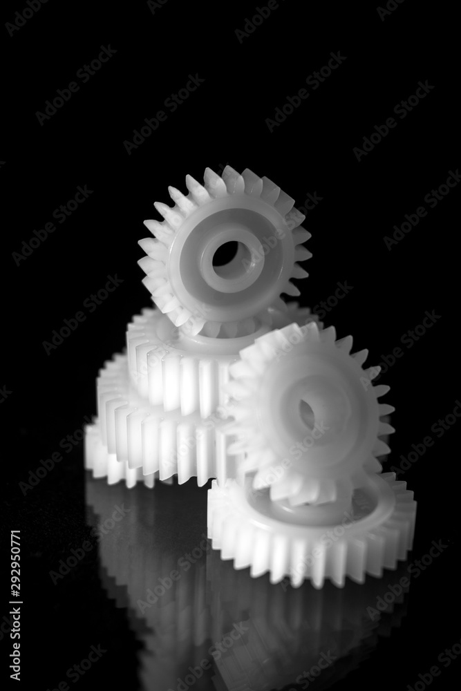 Several white plastic gears on a black mirror background. Mechanical repair. Fix. Reflection. Repair shop. Cogwheels. Elements of a large mechanism. Harmonious work. Several white plastic gears on a black mirror background. Mechanical repair. Fix. Reflection. Repair shop. Cogwheels. Elements of a large mechanism. Harmonious work.