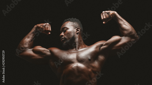 Athletic african fitness model flexing muscles over black studio background