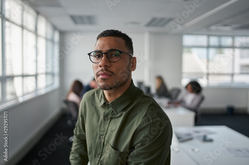 Portrait of a serious young professional businessman wearing eyeglasses looking at camera while colleague at background photo