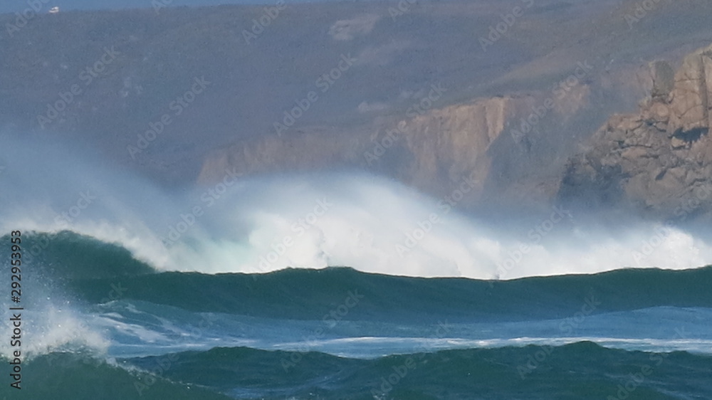 Fototapeta premium White horses riding electric blue waves at Sennen