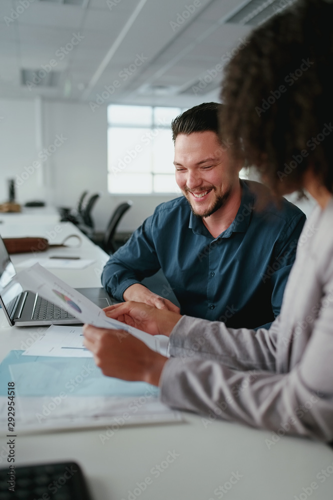 Close-up of a smiling young businessman sitting with his female colleague working with new startup project Close-up of a smiling young businessman sitting with his female colleague working with new startup project