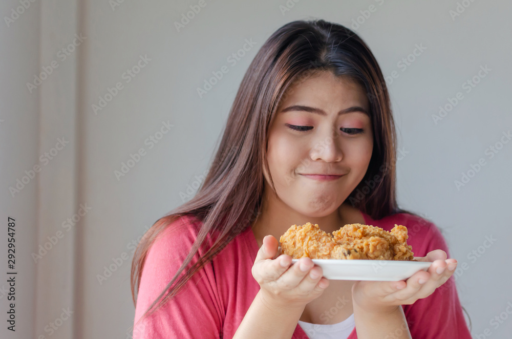 Asian young pretty woman slim body enjoying and holding delicious crispy fried chicken on dish in kitchen at home office, junk food, unhealthy food, dieting, weight loss and good healthy concept