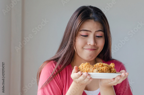 Asian young pretty woman slim body enjoying and holding delicious crispy fried chicken on dish in kitchen at home office  junk food  unhealthy food  dieting  weight loss and good healthy concept