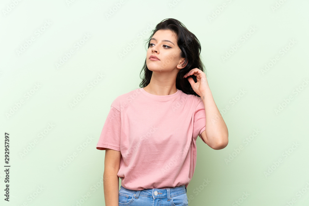 Young woman over isolated green background having doubts Young woman over isolated green background having doubts