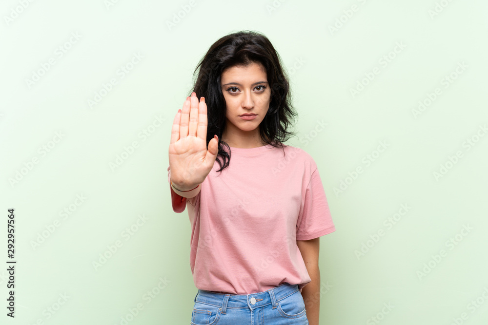 Young woman over isolated green background making stop gesture Young woman over isolated green background making stop gesture