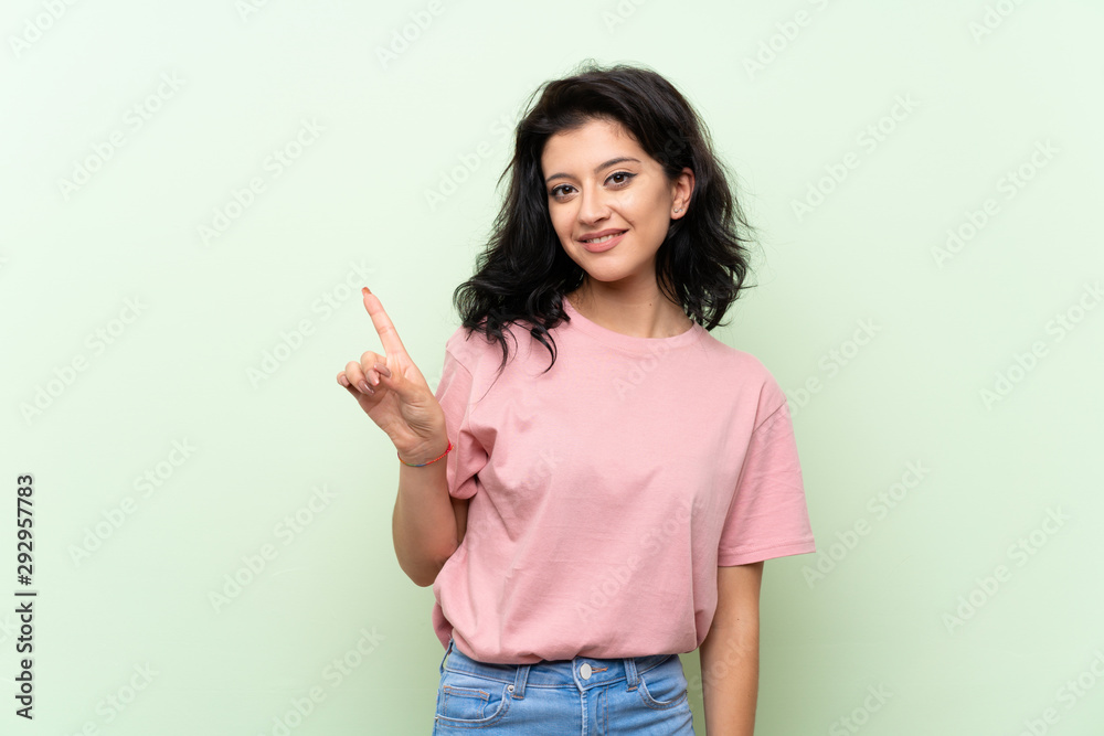 Young woman over isolated green background showing and lifting a finger in sign of the best Young woman over isolated green background showing and lifting a finger in sign of the best