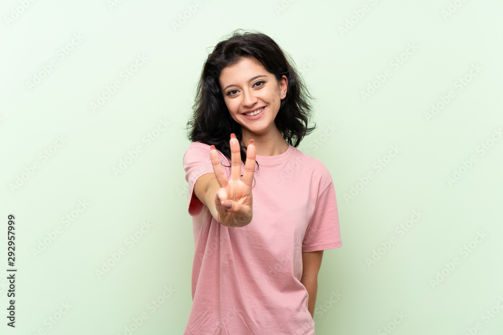 Young woman over isolated green background happy and counting three with fingers Young woman over isolated green background happy and counting three with fingers