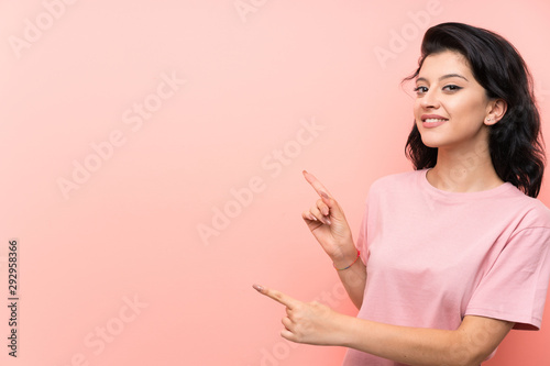 Young woman over isolated pink background pointing finger to the side