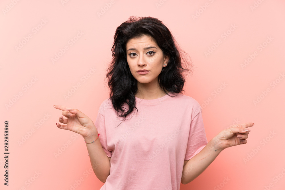 Young woman over isolated pink background pointing to the laterals having doubts Young woman over isolated pink background pointing to the laterals having doubts