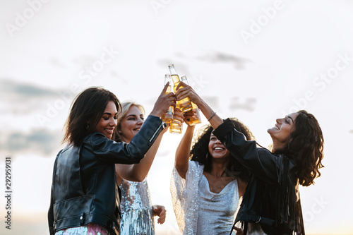 Four happy friends toasting with beer bottles at sunset
