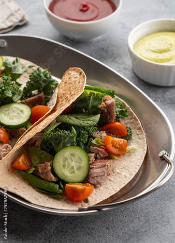 Two mexican pork carnitas tacos with sauces and vegetables.