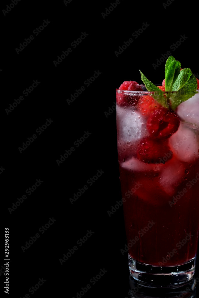 Red drink with ice, raspberries and mint in a tall glass against the black background Red drink with ice, raspberries and mint in a tall glass against the black background