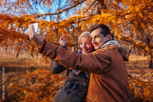 Adult son taking selfie with his mother using smartphone in autumn park. Family time © maryviolet
