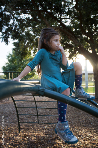 A little girl sitting atop a jungle gym outside at a playground