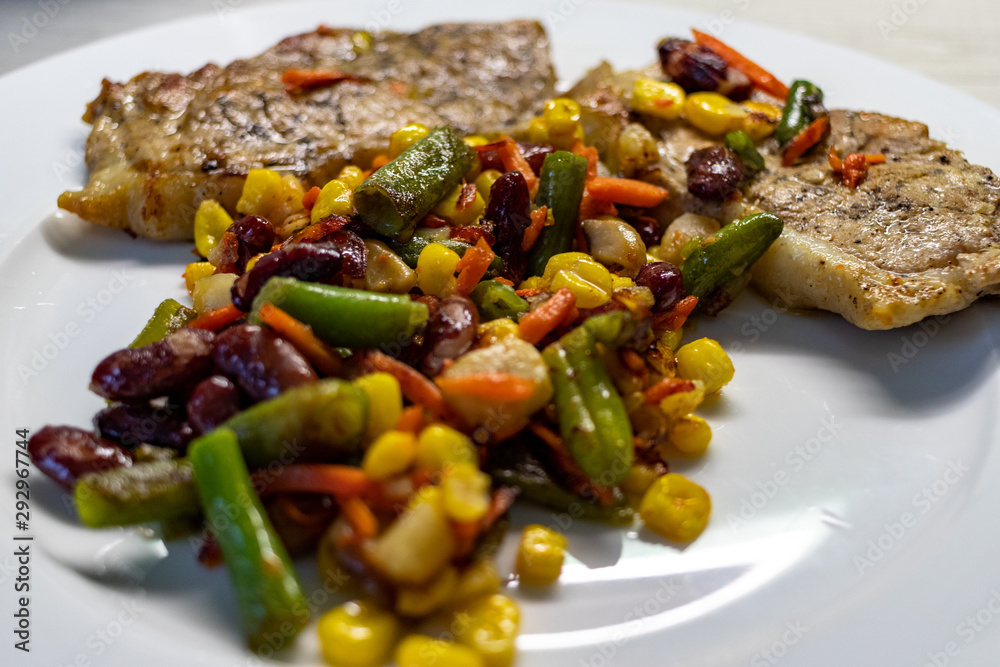 Mix of vegetable with fried meat on white plate of the light table. Mix of vegetable containing carrots, peas, beans and corn. Fried pork on a plate Mix of vegetable with fried meat on white plate of the light table. Mix of vegetable containing carrots, peas, beans and corn. Fried pork on a plate