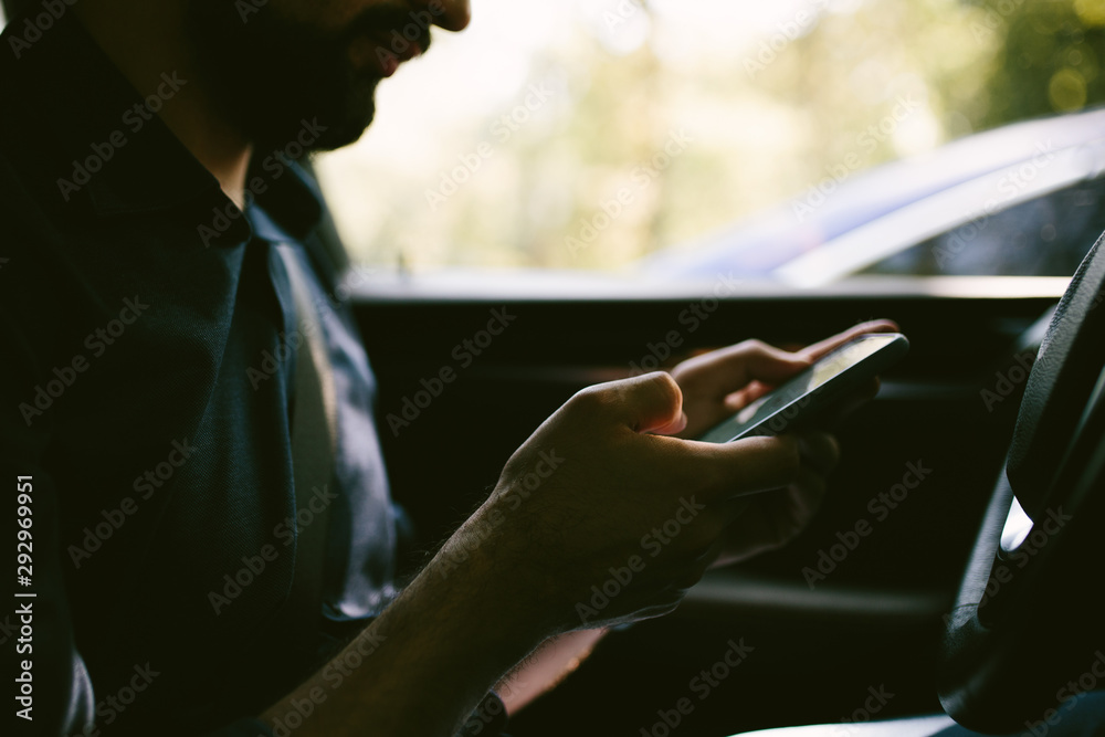 Man texting a messsage in a mobile phone while sitting in a car.  Close up shot