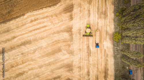 A beautiful new combine harvester dumps grain into a truck trailer on the field. Aerial view