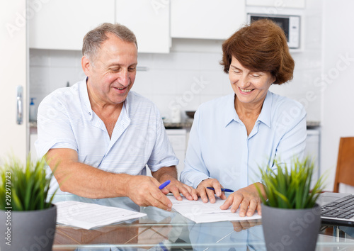 Mature family couple sitting at kitchen table and signing documents