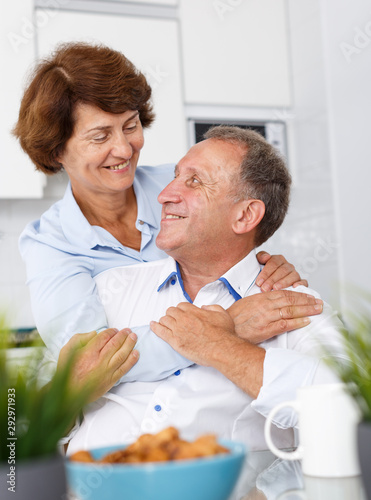 Mature family couple hugging at kitchen table during drinking tea