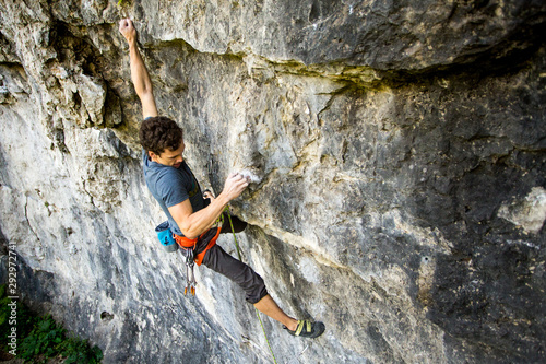 Fototapet Strong rock climber holding onto tiny little holds