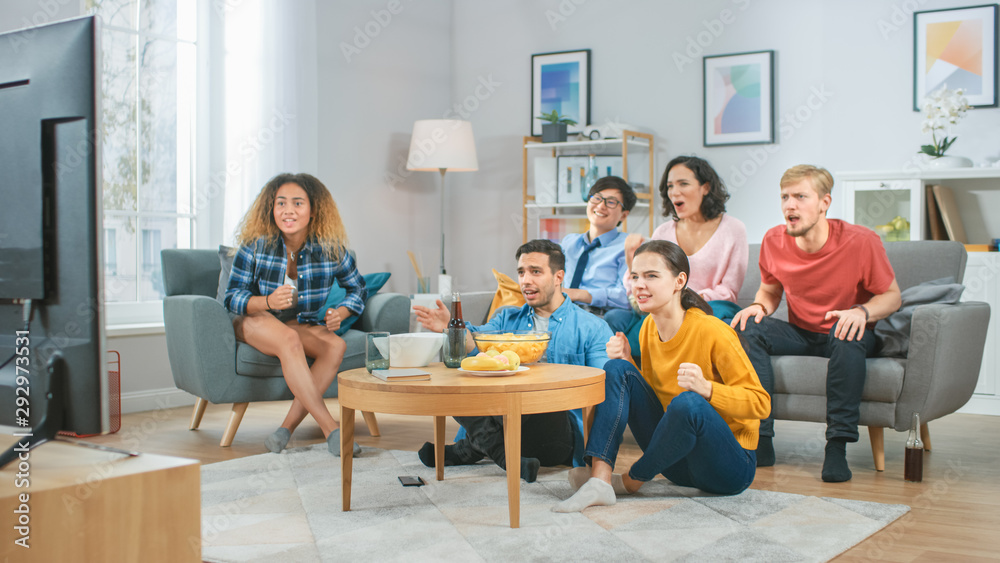 At Home Diverse Group Friends Watching TV Together, Eating Snacks and Drinking Beverage. They Probably Watching Sports Game or Fun Movie. At Home Diverse Group Friends Watching TV Together, Eating Snacks and Drinking Beverage. They Probably Watching Sports Game or Fun Movie.
