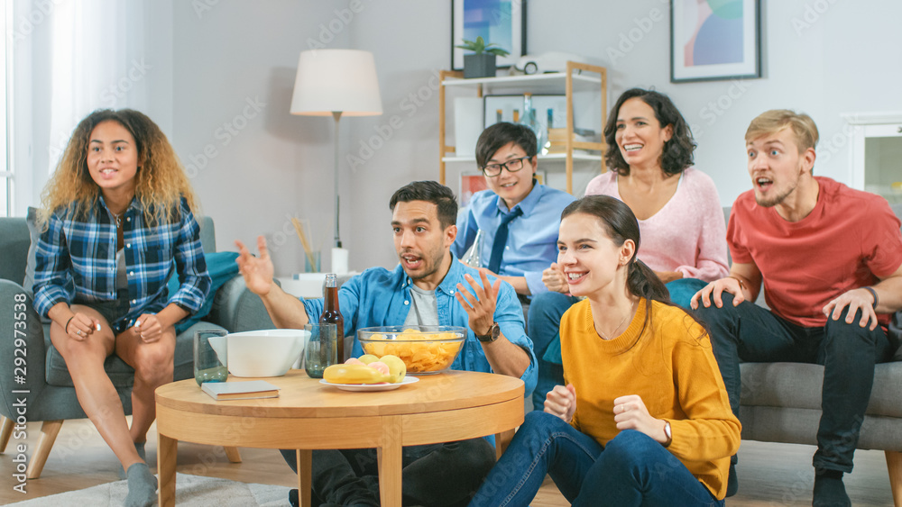 At Home Diverse Group Friends Watching TV Together, Eating Snacks and Drinking Beverage. They Probably Watching Sports Game or Fun Movie. At Home Diverse Group Friends Watching TV Together, Eating Snacks and Drinking Beverage. They Probably Watching Sports Game or Fun Movie.