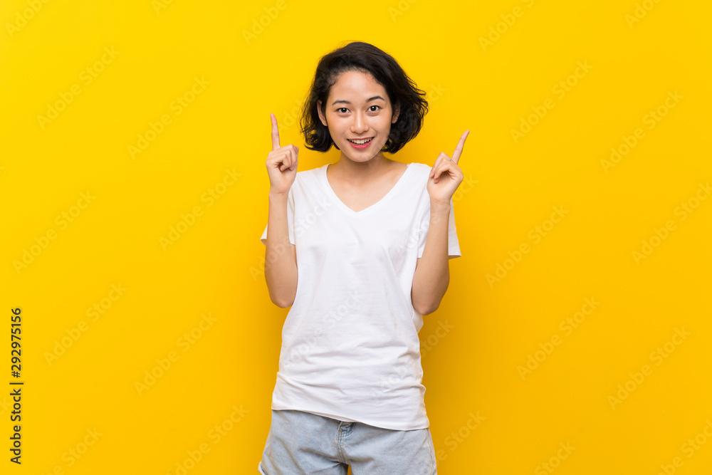 Asian young woman over isolated yellow wall pointing up a great idea Asian young woman over isolated yellow wall pointing up a great idea
