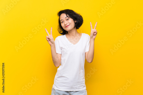 Asian young woman over isolated yellow wall showing victory sign with both hands
