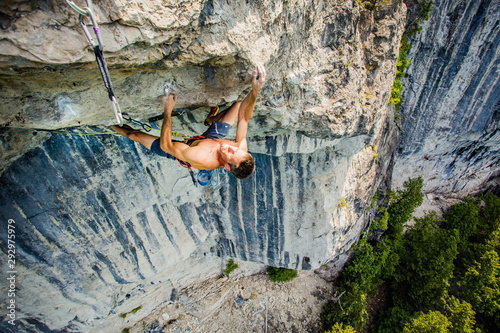 Shirtless fit man hanging on one finger high up under a roof of rock