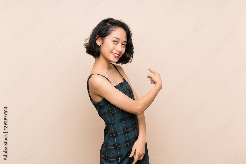 Asian young woman over isolated yellow wall pointing back Asian young woman over isolated yellow wall pointing back