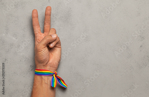 Symbol of peace and victory from two fingers. Grey background. LGBT rainbow ribbon pride. Copy space for text. photo