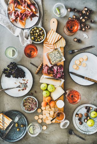 Mid-summer picnic with wine and snacks. Flat-lay of charcuterie and cheese board, rose wine, nuts, olives and fruits over concrete table background, top view