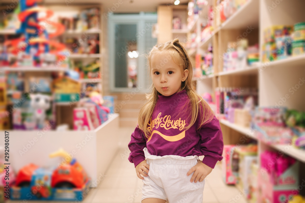 Adorable little girl shopping for toys. Cute female in toy store. Happy young girl selecting toy Adorable little girl shopping for toys. Cute female in toy store. Happy young girl selecting toy