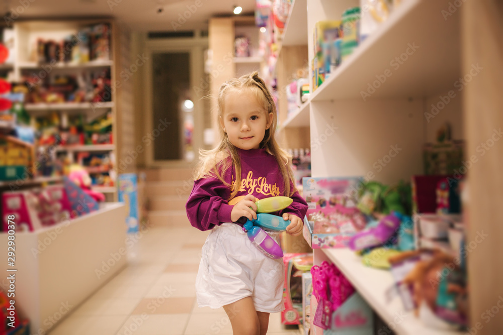 Adorable little girl shopping for toys. Cute female in toy store. Happy young girl selecting toy Adorable little girl shopping for toys. Cute female in toy store. Happy young girl selecting toy