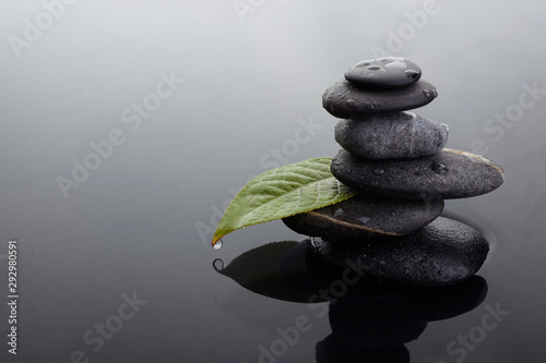 Zen stones in balanced pile and green leaf with water drops in water