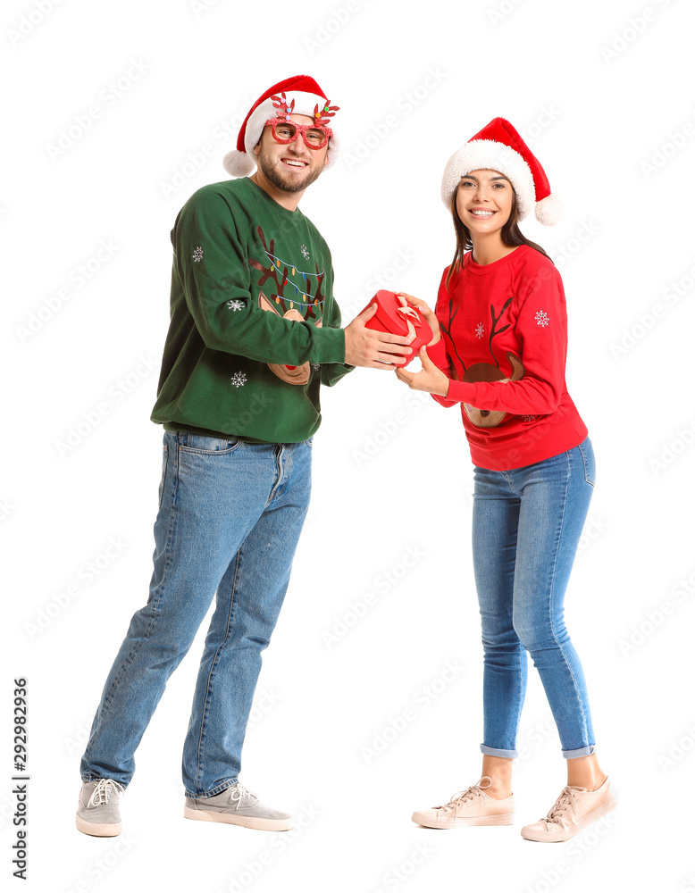 Young couple in Christmas sweaters and with gift on white background