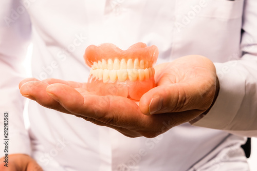 A dentist doctor in a white coat holds a false jaw in his hands. The concept of healthy teeth.